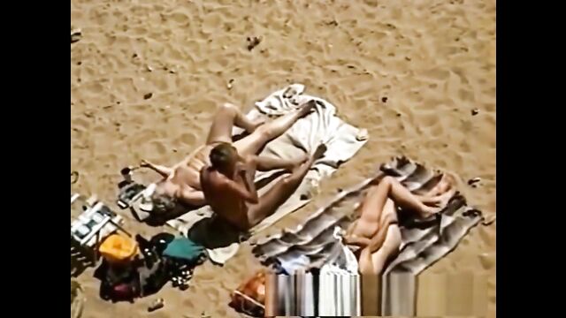 A couple is being watched while getting intimate on the beach by strangers