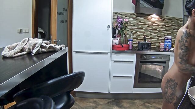 A tatooed woman is cooking without any clothes on